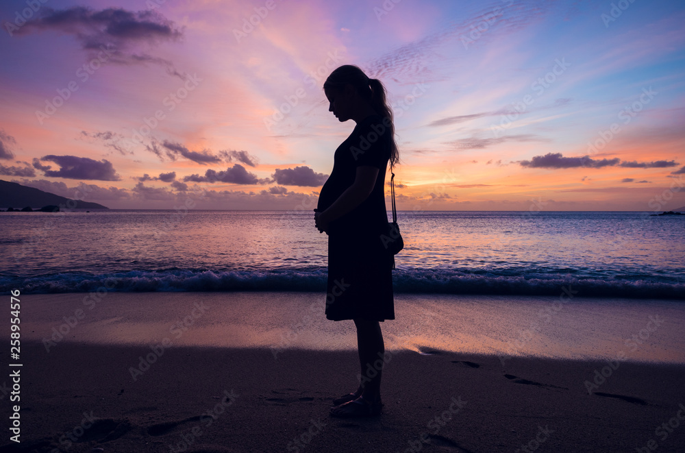 A silhouette of a pregnant girl on a beautiful tropical beach at sunset dusk, relaxation and positive mental health during pregnancy for women. Healthy mind.