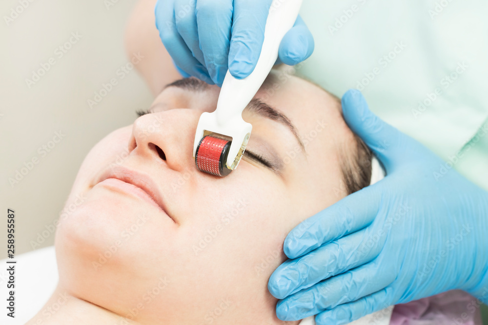 The woman undergoes the procedure of medical micro needle therapy with a modern medical instrument derma roller. The woman undergoes the procedure of medical micro needle therapy with a modern medical instrument derma roller.