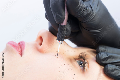 Permanent microblading tattooing freckles to a woman in a beauty salon