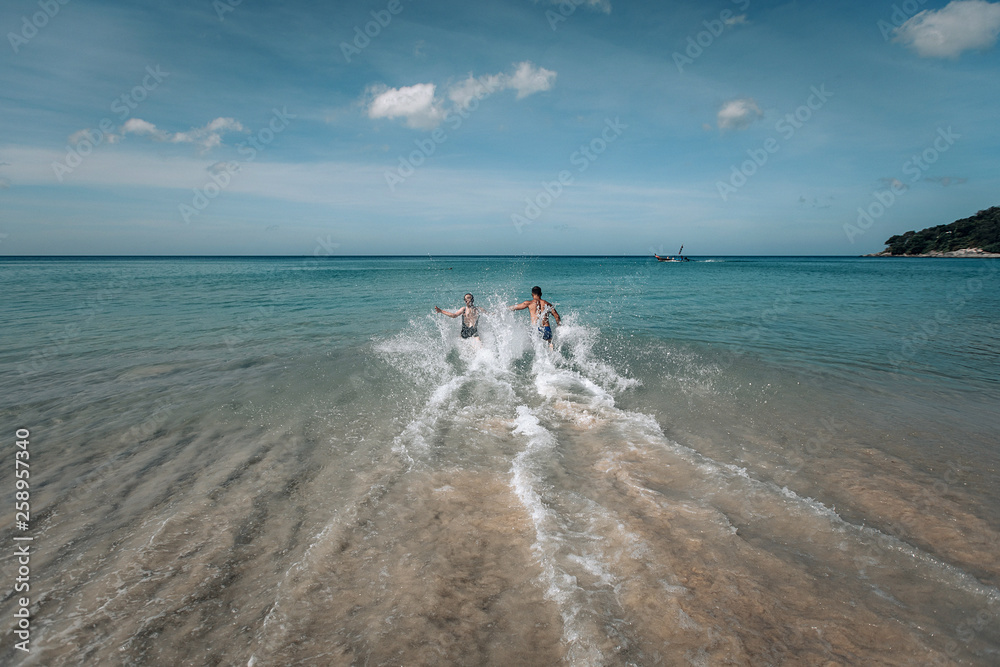 Sexy couple in the water.Big sea waves. Beautiful blonde in black swimsuit with long hair and a man are on vacation. Phuket. Thailand.