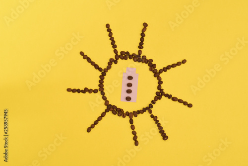 Funny and cute sun from coffee beans with battery inside on a yellow background
