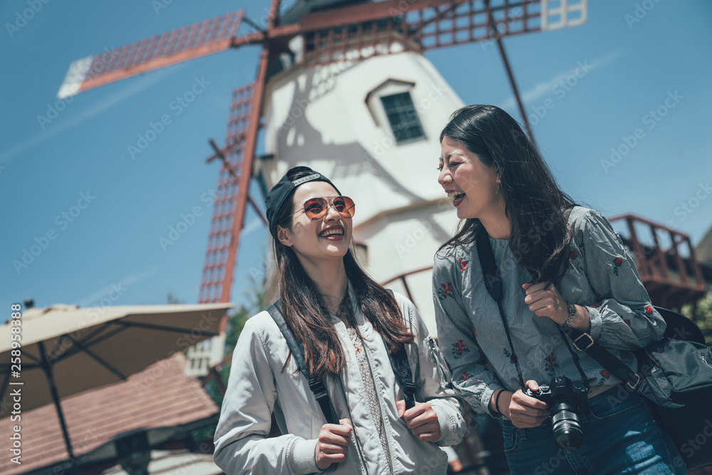 © PR Image Factory - two joyful asian women tourist travel with camera in solvang santa barbara california america. young girl best friends travel together smiling sightseeing windmill outdoor under blue sky in summer