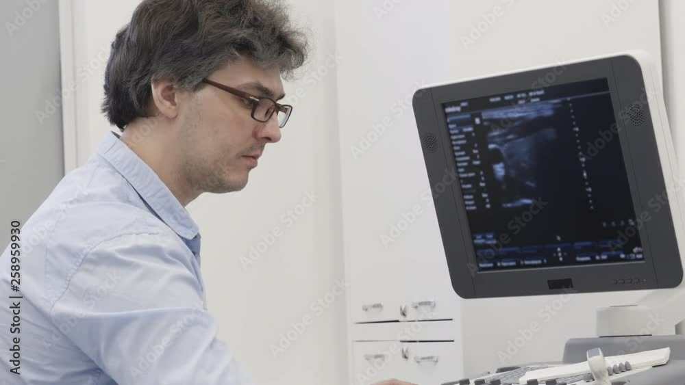 Professional ultrasonography doctor detect the disease at ultrasound examine using supersonic computerized tool equipment from latest diagnostic system. Concentrated adult man looking at monitor Professional ultrasonography doctor detect the disease at ultrasound examine using supersonic computerized tool equipment from latest diagnostic system. Concentrated adult man looking at monitor