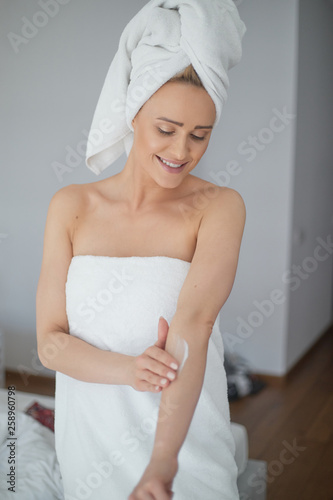 Middle aged beautiful blond woman moisturizes arm after the shower