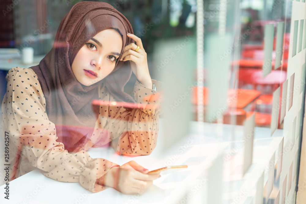 Young asian muslim business woman in brown hijab casual wear sitting in the creative cafe. Young asian muslim business woman in brown hijab casual wear sitting in the creative cafe.