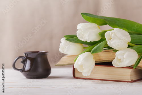 White tulips, old books, a Cup of coffee in the distance on a beige background. Morning, spring, reading, coffee break
