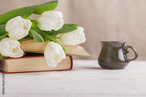 White tulips  old books  a Cup of coffee in the distance on a beige background. Morning  spring  reading  coffee break