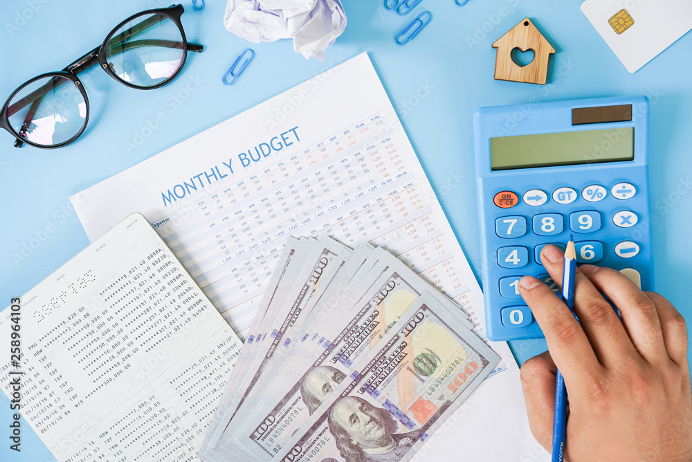 Hand using calculator calculating monthly budget with passbook and us