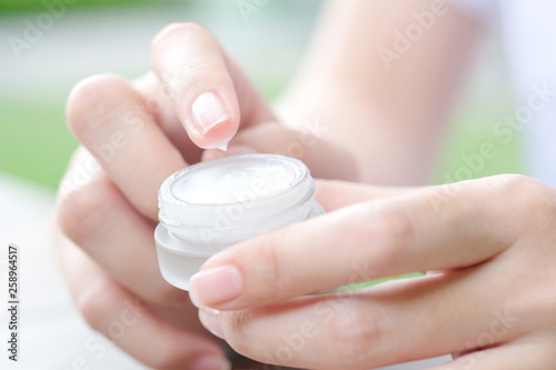 Hand of woman holding moisturizer cream and serum. She applying a facial cream   essential   oil   lotion and body cream for skin care  close up view and blur background. Beauty and Healthy Concept.