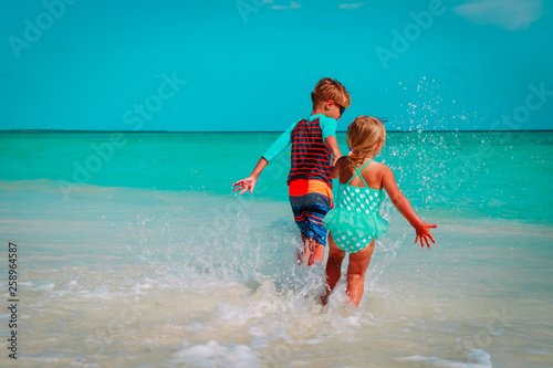 little girl and boy run play with water on beach