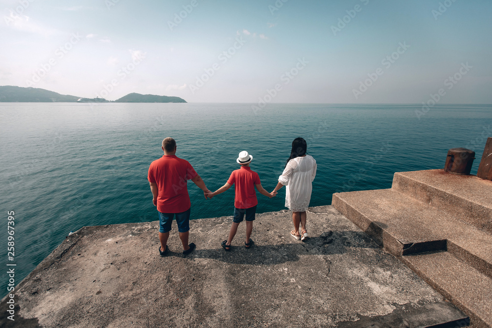 Happy family on pier. Back view. Man, woman and son holding hands and standing near the sea. summer vacation. Phuket. Thailand