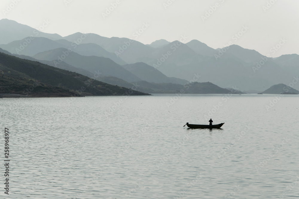 Silhouette of a fisherman in small boat in lake, Albania Silhouette of a fisherman in small boat in lake, Albania