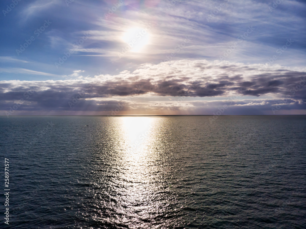 Obraz premium Aerial view above ocean, with cloudy pastel colored scenic sky and sun rays hits the water in a hot summer day