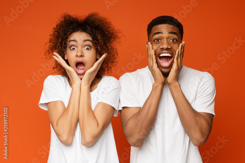 Amazed black man and woman opening mouths and touching cheeks