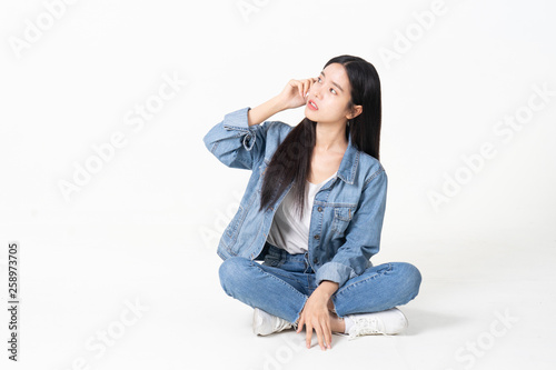 Thinking asian woman sitting on floor isolated on white background.Asian female model smiling looking up.woman pointing fingers away while sitting on a floor with legs crossed isolated