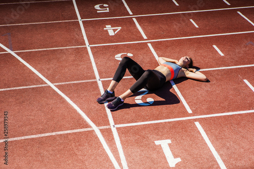 From above view of exhausted teen athlete in sportswear resting on track after finishing tough race