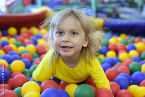 Portrait of a blond boy in a yellow t-shirt. The child smiles and plays in the children's playroom. Ball pool.