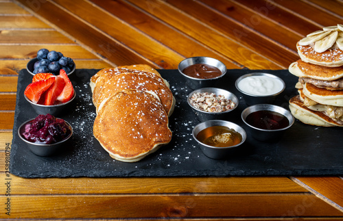 platter of pancakes with . double large stack of protein pancakes and array of different toppings on the side including strawberries blueberries maple syrup granola and sour cream 