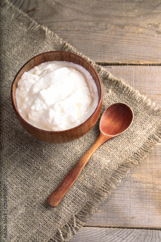 Yogurt in wooden bowl with wooden spoon on burlap on wooden table. Yogurt in wooden bowl with wooden spoon on burlap on wooden table.