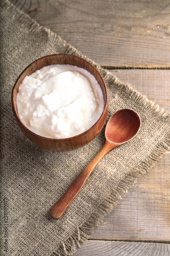 Yogurt in wooden bowl with wooden spoon on burlap on wooden table. 