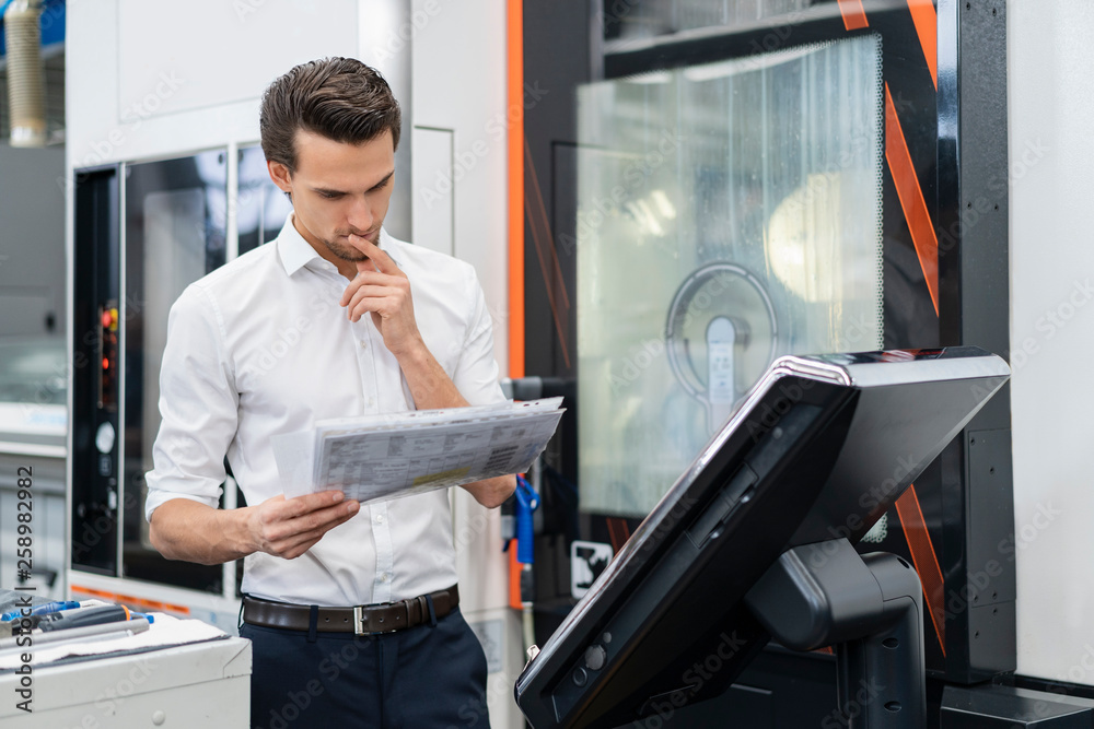 Businessman reading manual at a machine in a factory Businessman reading manual at a machine in a factory