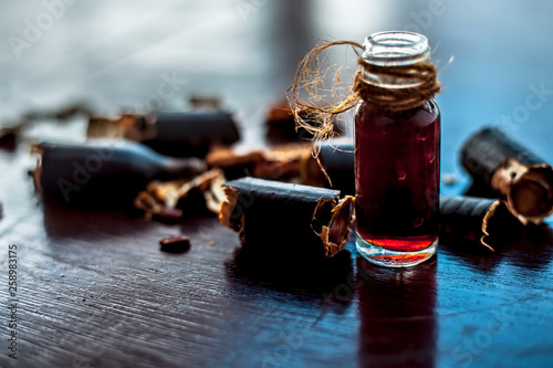 Golden shower tree or garmalo or Amaltas or Cassia fistula oil in a transparent glass bottle along with its fruit and cut pulp on wooden surface. photo