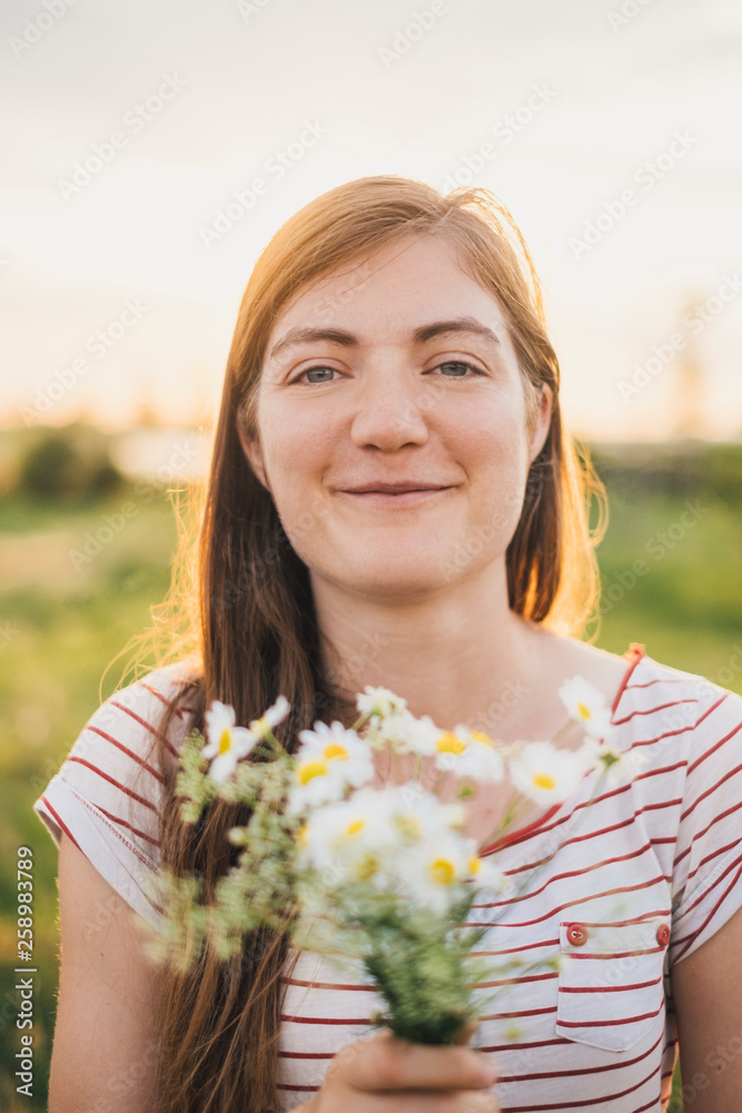 Portrait of smiling young woman holding bunch of picked wildflowers Portrait of smiling young woman holding bunch of picked wildflowers