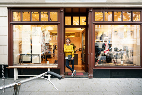 Young woman standing in door of a fashion store, holding laptop photo