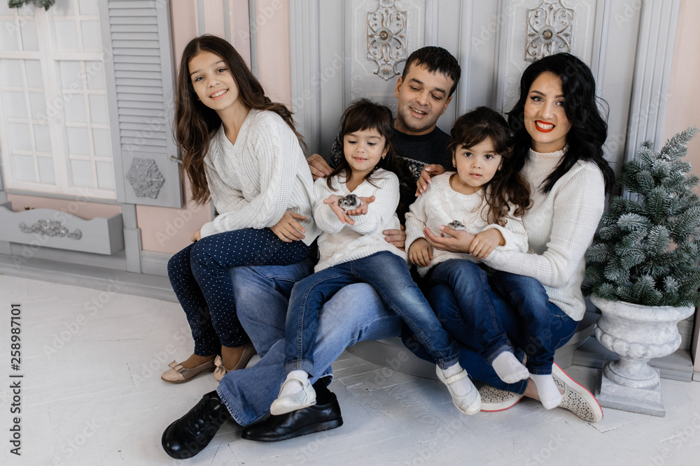Charming family of nice couple with three charming children in blue jeans poses in cozy room with Christmas decor Charming family of nice couple with three charming children in blue jeans poses in cozy room with Christmas decor