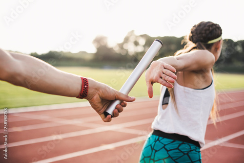 Close up of athlete hand passing baton to woman running on track photo