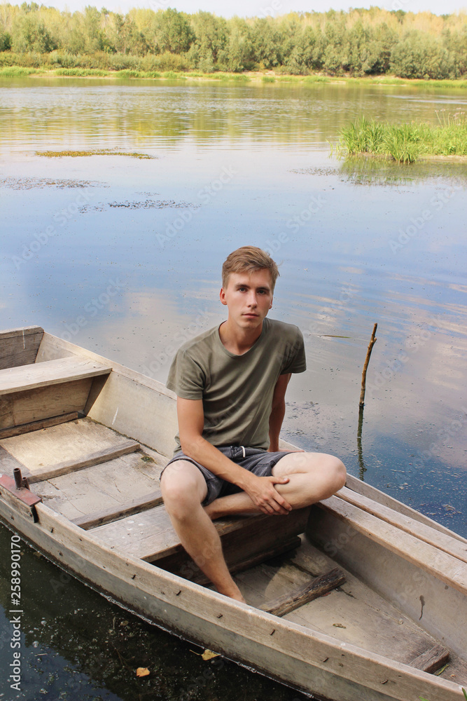 village vacations: a young man sits in a boat in the middle of a river village vacations: a young man sits in a boat in the middle of a river