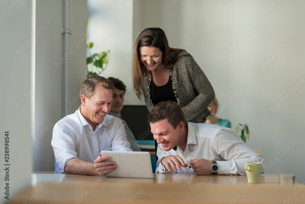 Happy colleagues looking at tablet in office Happy colleagues looking at tablet in office