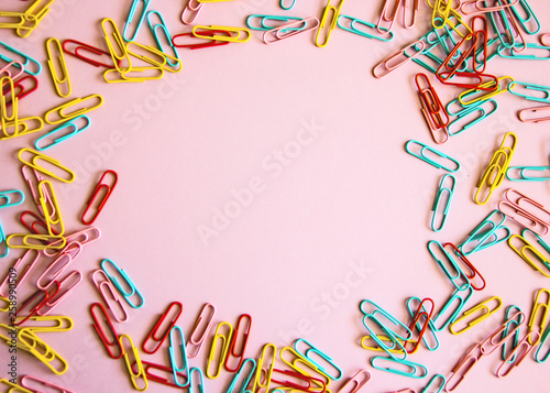 Pink background with colored stationery for paper scattered on it. paper clips on a pink background, office theme. Colorful Back to School background. Top view, flat lay.