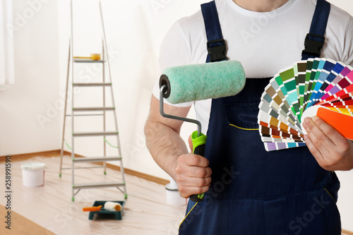 Male decorator with paint roller and color palette samples in empty room, closeup. Space for text photo