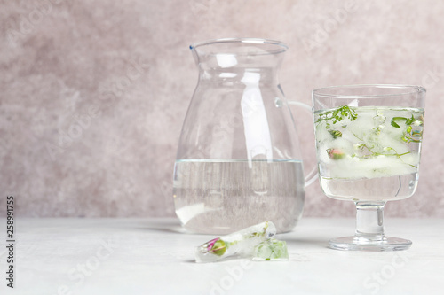 Glass with floral ice cubes and water near jug on table. Space for text