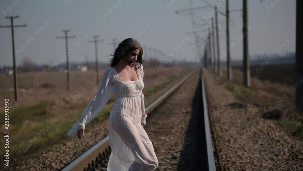 Portrait amazing slim unusual girl in white translucent dress and with makeup on her face in form of torn bloody wound makes unusual dance moves on railway tracks in sunny day Portrait amazing slim unusual girl in white translucent dress and with makeup on her face in form of torn bloody wound makes unusual dance moves on railway tracks in sunny day