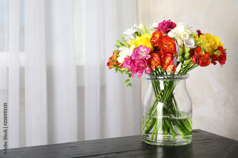 Vase with bouquet of spring freesia flowers on table in room. Space for text Vase with bouquet of spring freesia flowers on table in room. Space for text
