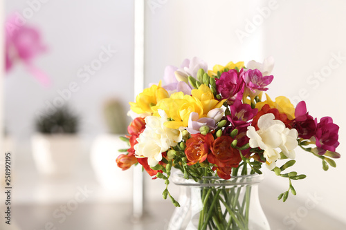 Vase with bright spring freesia flowers on table. Space for text