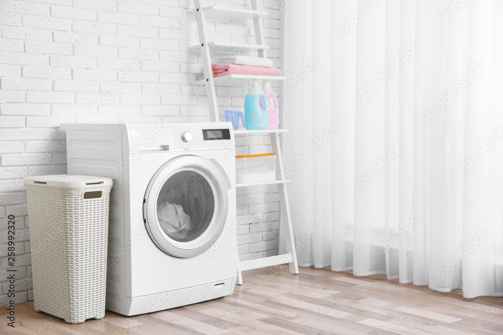Modern washing machine near brick wall in laundry room interior, space for text