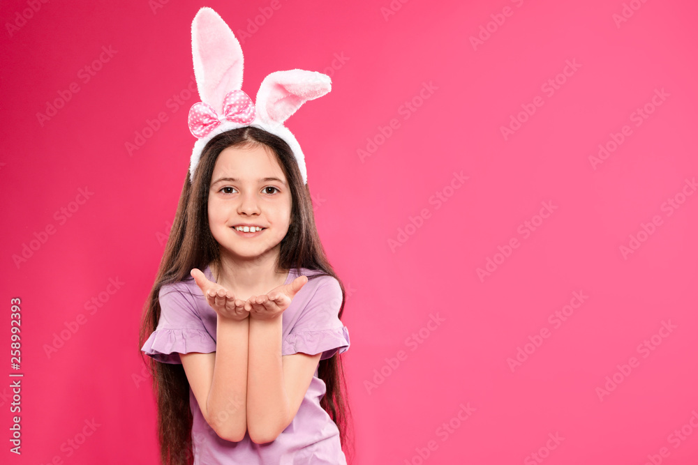 Portrait of little girl in Easter bunny ears headband on color background, space for text