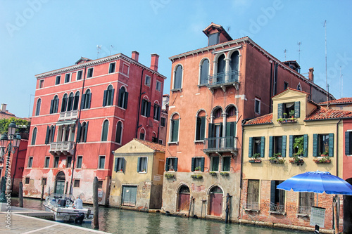 a cozy little beautiful water canal in Venice with colorful old red and orange plaster stucco houses and greenery on facades in Italy