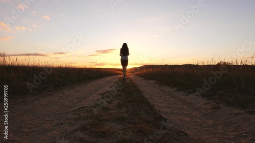 A business woman walks along a country road with a tablet in her hand, the sun miertsaet between women's legs. sexy business woman girl running in the countryside. sexy girl travels in countryside