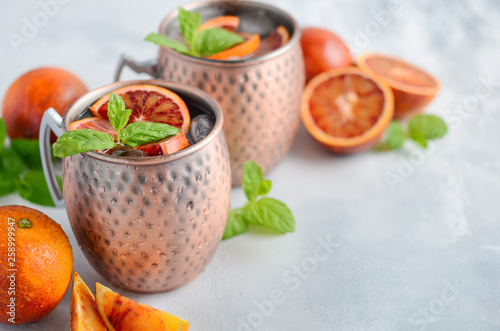 Photography Blood orange Moscow mule alcohol cocktail with fresh mint leaves and ice in copper mugs on a gray concrete background
