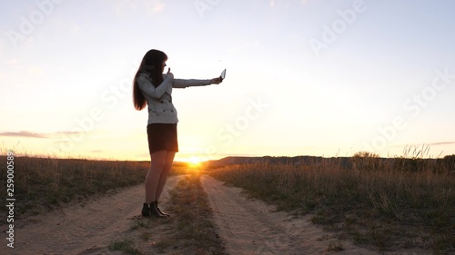 beautiful business woman travels and takes a selfie photo using mobile smartphone on the road against the sunset. concept of tourism. Girl tourist in the field makes selfie with tablet