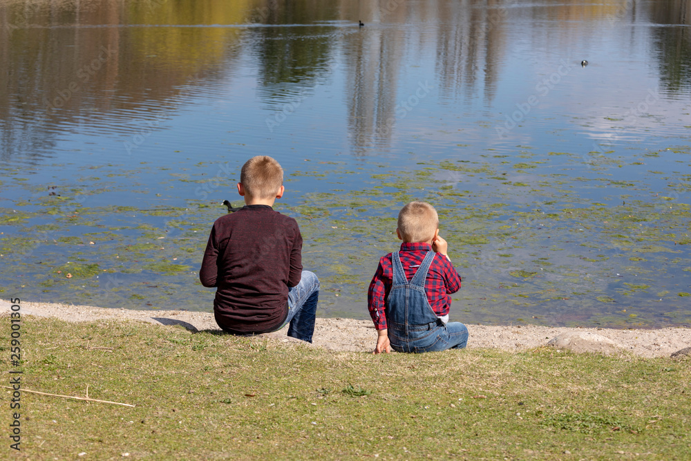 Fototapeta premium Children sit together at the lake and look out to the water