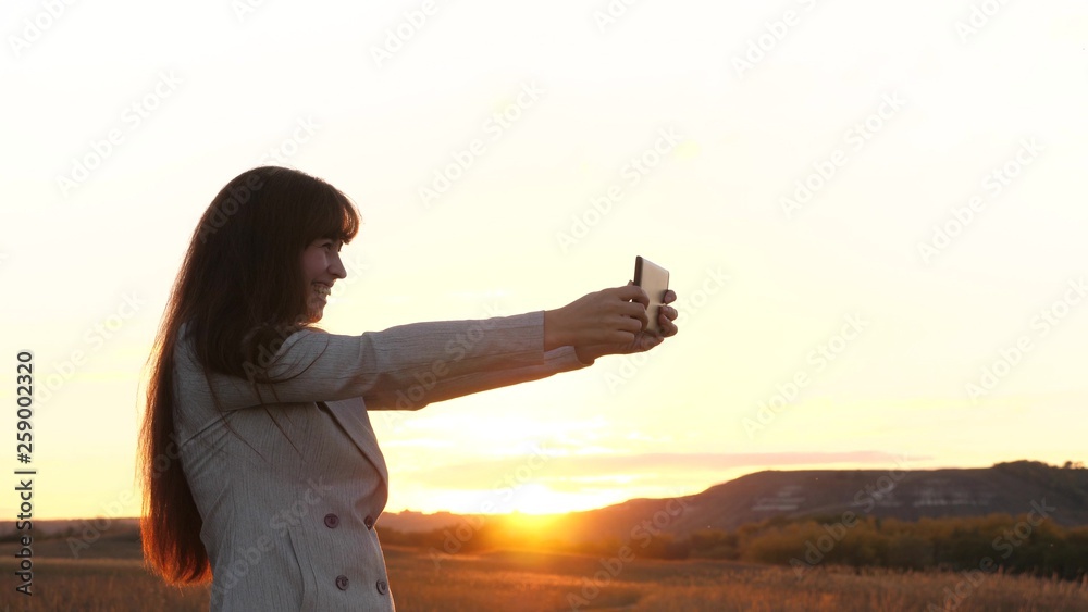 Girl tourist in the field makes selfie with tablet. beautiful business woman travels and takes a selfie photo using mobile smartphone against the backdrop of the sunset. concept of tourism