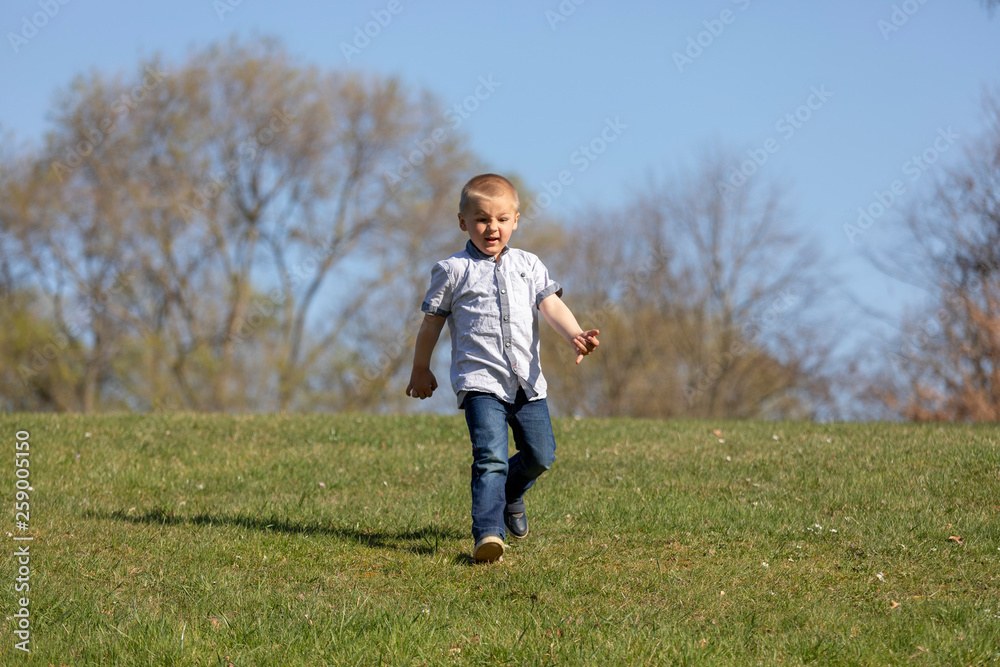 Cute boy running across grass und smiling.