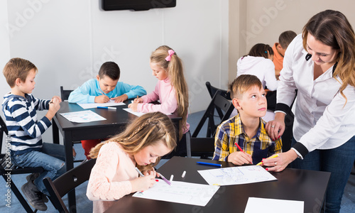 Little children with friendly teacher drawing in classroom