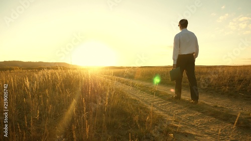 businessman goes on a country road with a briefcase in his hand. The entrepreneur works in a rural area. farmer inspects his land in the evening at sunset. agricultural business concept. © zoteva87