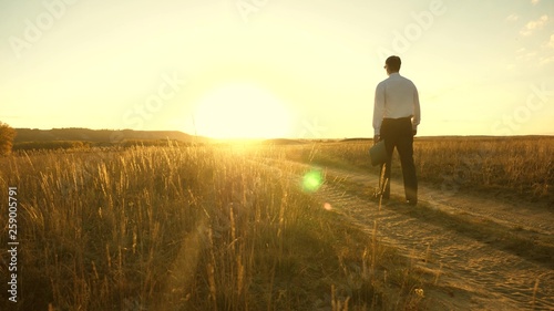 businessman goes on a country road with a briefcase in his hand. The entrepreneur works in a rural area. farmer inspects his land in the evening at sunset. agricultural business concept.